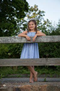 Young girl in blue dress leaning on fence at beach