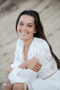 Senior portrait brunette in off white flowing dress at beach