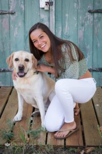 Teen girl in white pants green top by barn doors with yellow lab