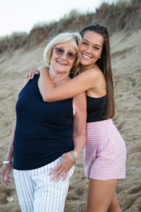Teen girl hugging grandmother in blue top at beach