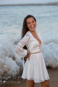 Teen girl in white dress at water's edge with waves crashing behind