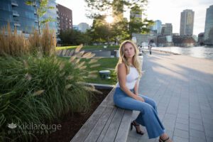 Blonde girl Boston Seaport sidewalk with white top and flare jeans sitting