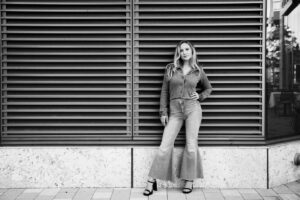 Girl in denim flare blonde hair leaning on black corrugated wall Seaport