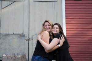 Two girls in black hugging in front of barn door