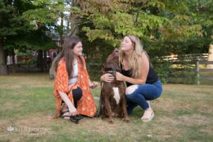 Two girls on grass playing with their cute brown dog
