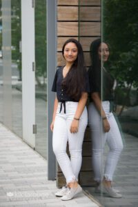 Full body portrait of teen girl in white pants against ICA building glass