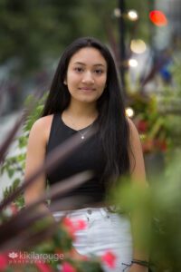 Serious portrait girl long hair in black top through plants
