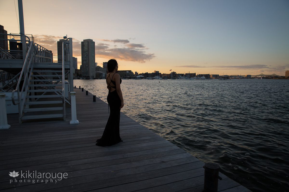 Girl in black prom dress silhouette with Boston Harbor