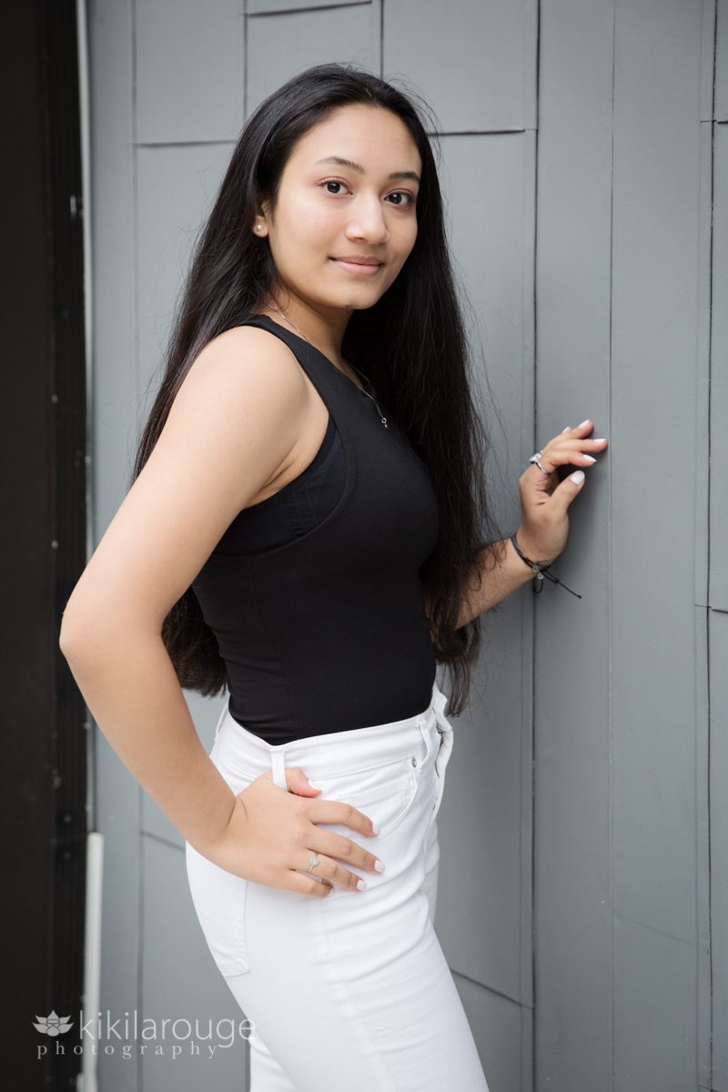 Serious portrait teen girl in white pants black top leaning city gray wall Boston