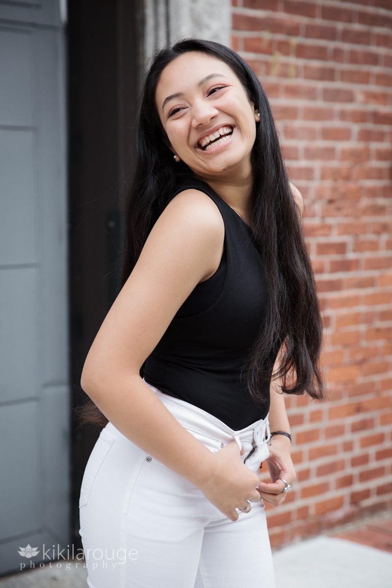 Teen girl laughing by brick wall Boston white jeans