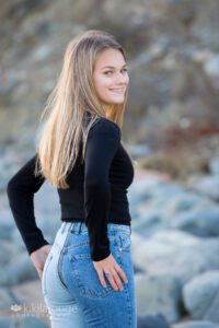 Pretty blonde Senior girl looking over shoulder by rocks at beach