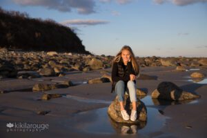 Girl sitting on lone rock with reflection at gorgeous open beach