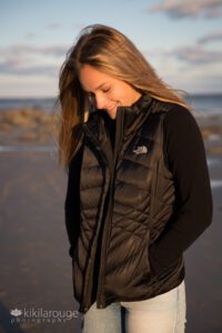 Girl in black puffer vest looking down smiling at wide open beach Sandy Point