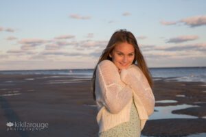 Girl hugging white sweater at water's edge keeping warm at beach