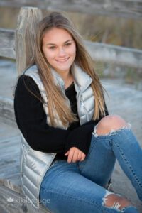 Teen girl sitting on Sandy Point boardwalk with jeans, black top and silver vest