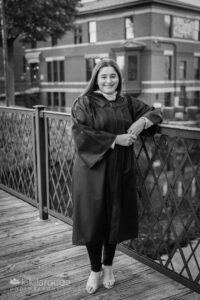 Graduate in gown leaning on riverwalk bridge UMass Lowell