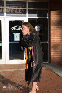Woman holding face in disbelief at ULowell in graduation gown