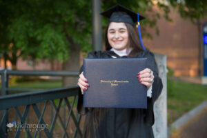 Girl long dark hair in cap and gown holding out diploma