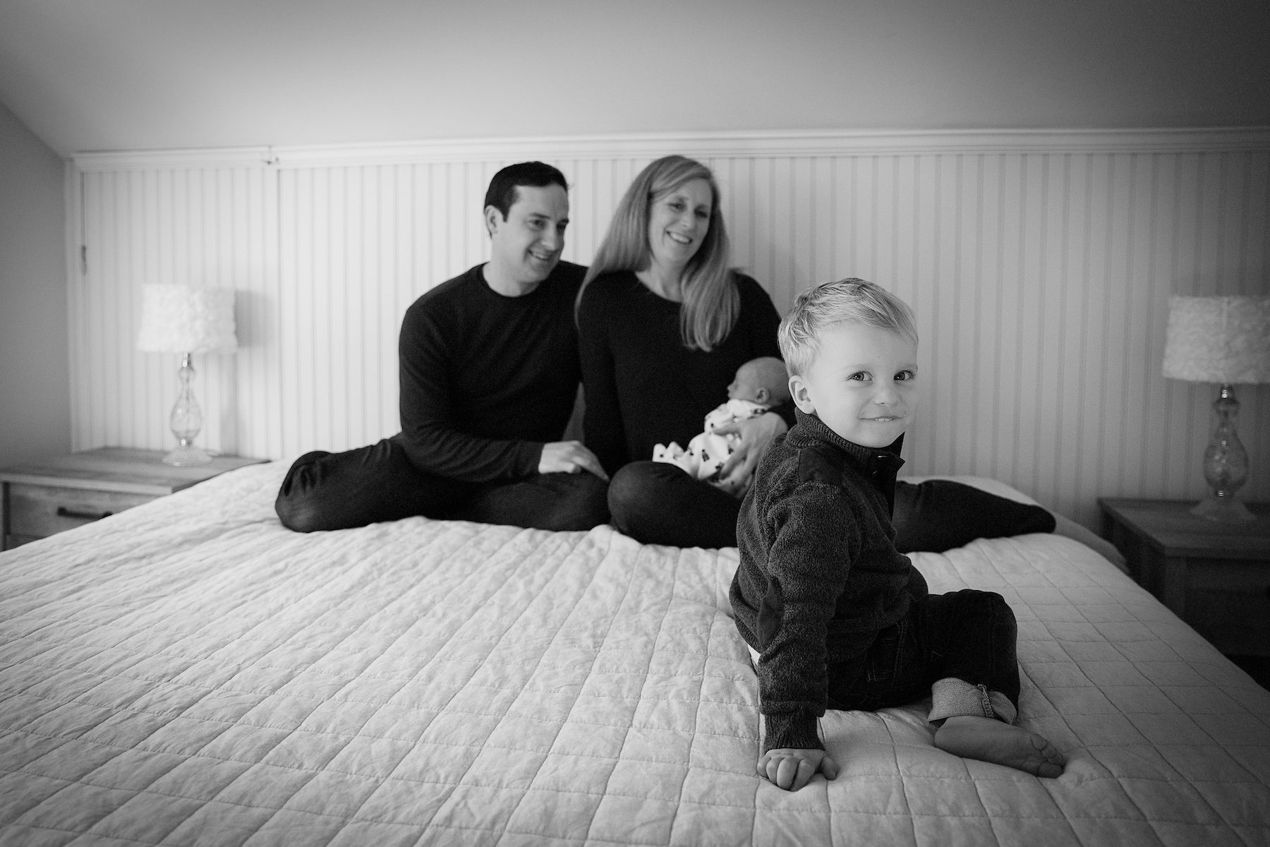 Mom and Dad with newborn and toddler sitting on bed