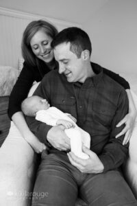Mom and Dad looking down a sleeping baby girl in chair