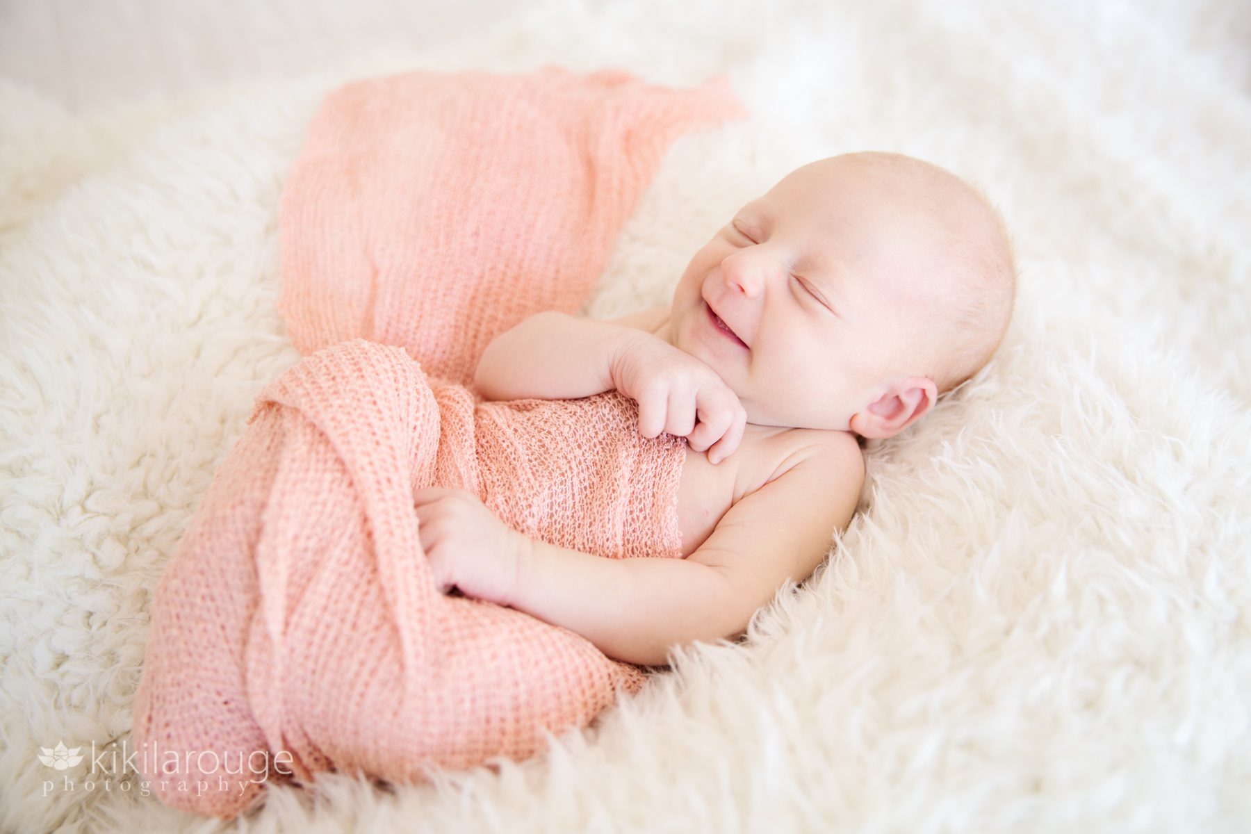 Newborn baby girl with big smile eyes closed in a peach wrap