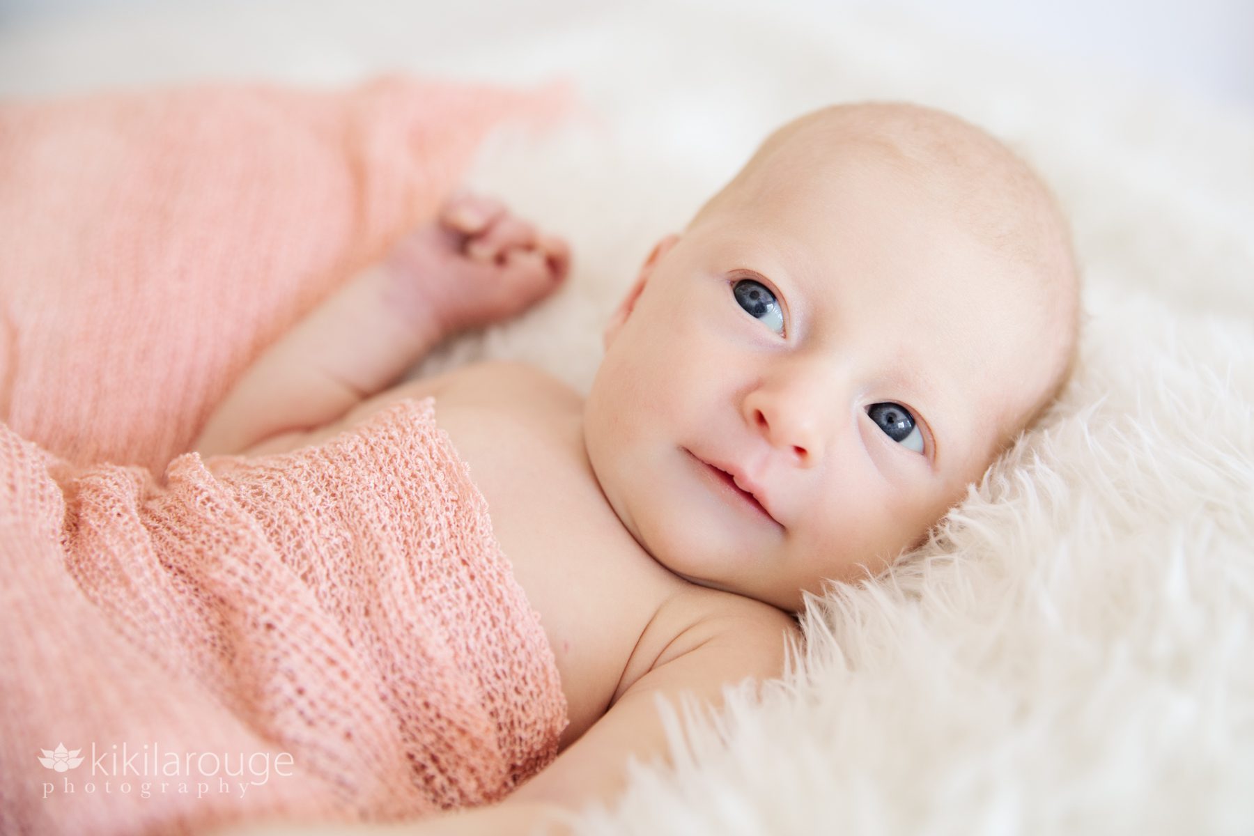 Newborn baby girl big blue eyes snuggled in white wrap
