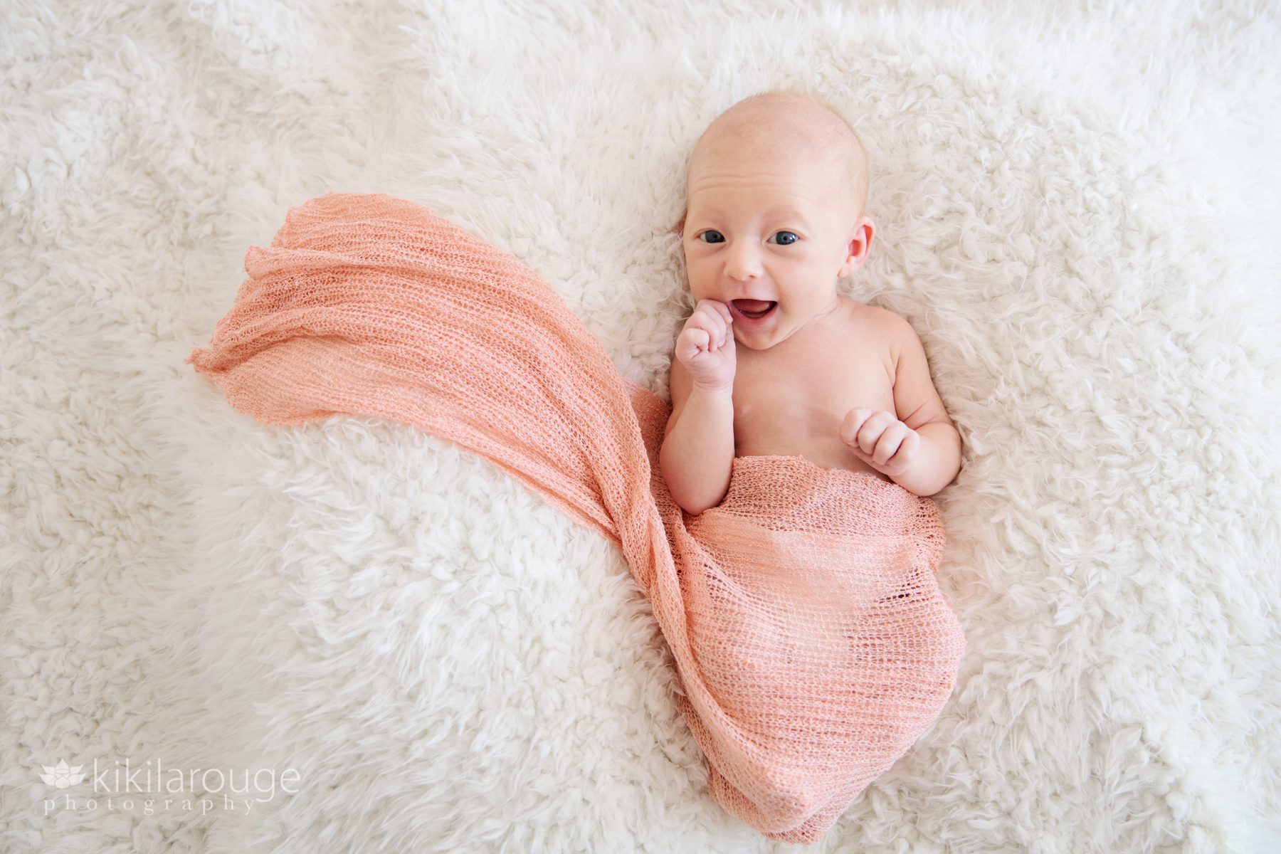 Smiling newborn baby girl in peach wrap on soft white blanket