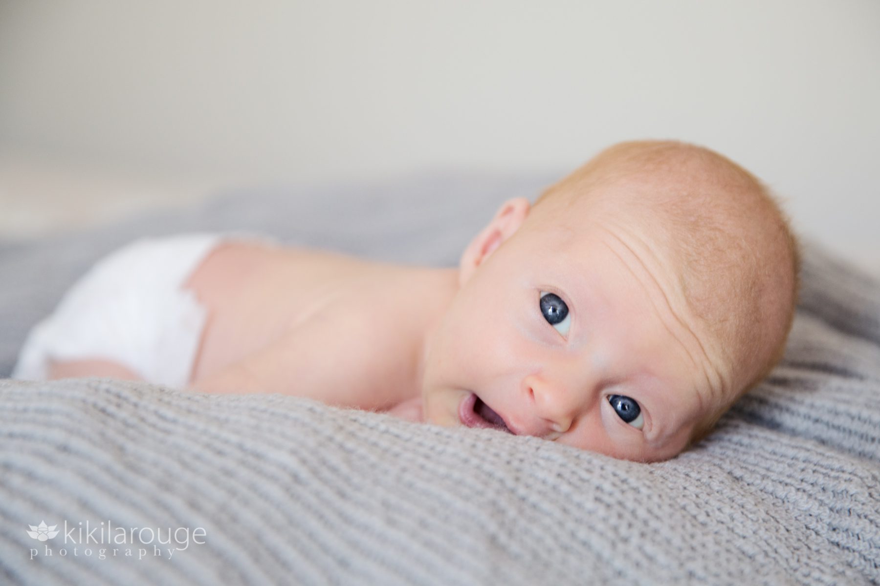 Newborn baby in white diaper with big blue eyes open