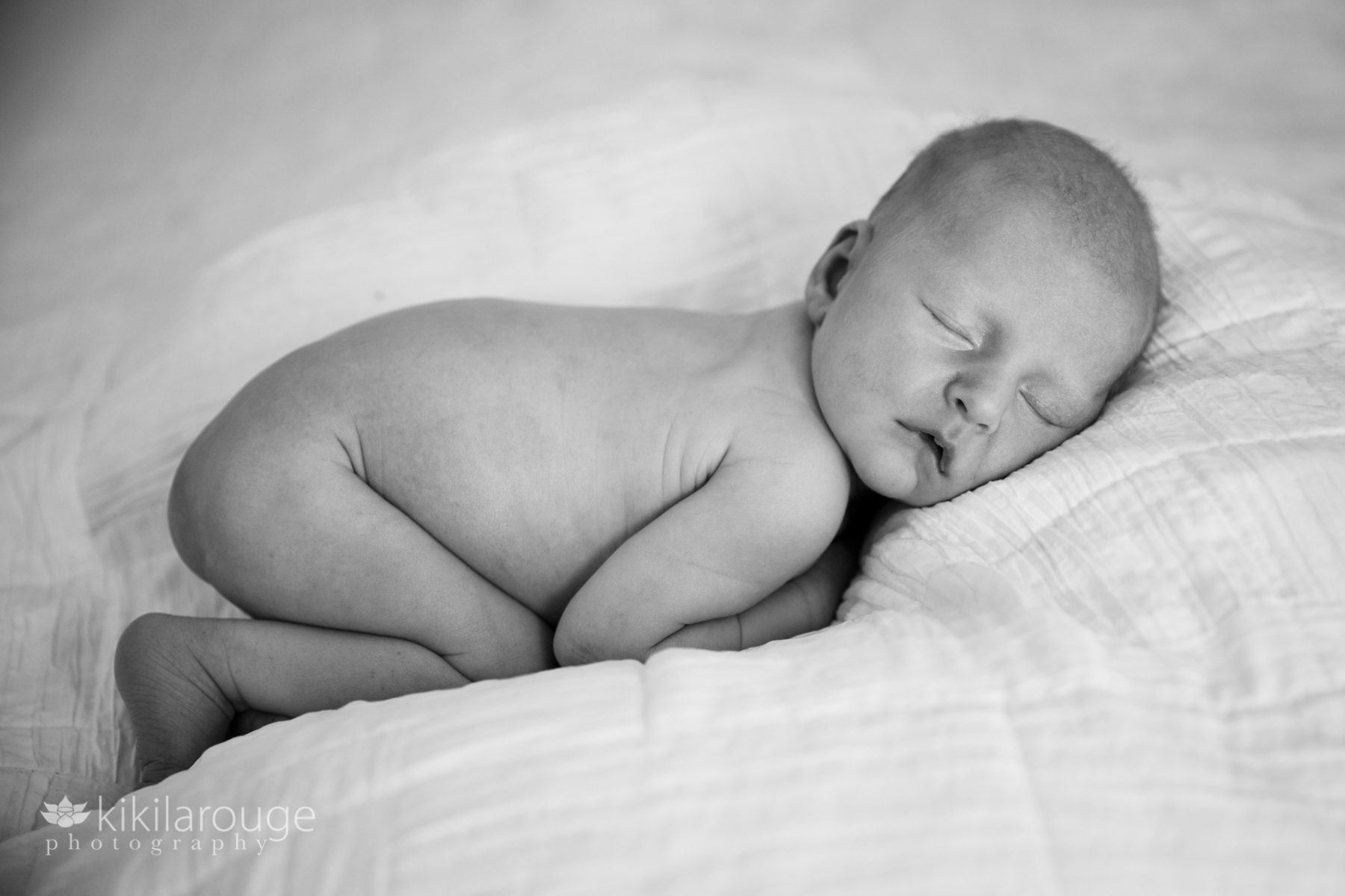 Tiny naked newborn baby snuggled up on bed sleeping
