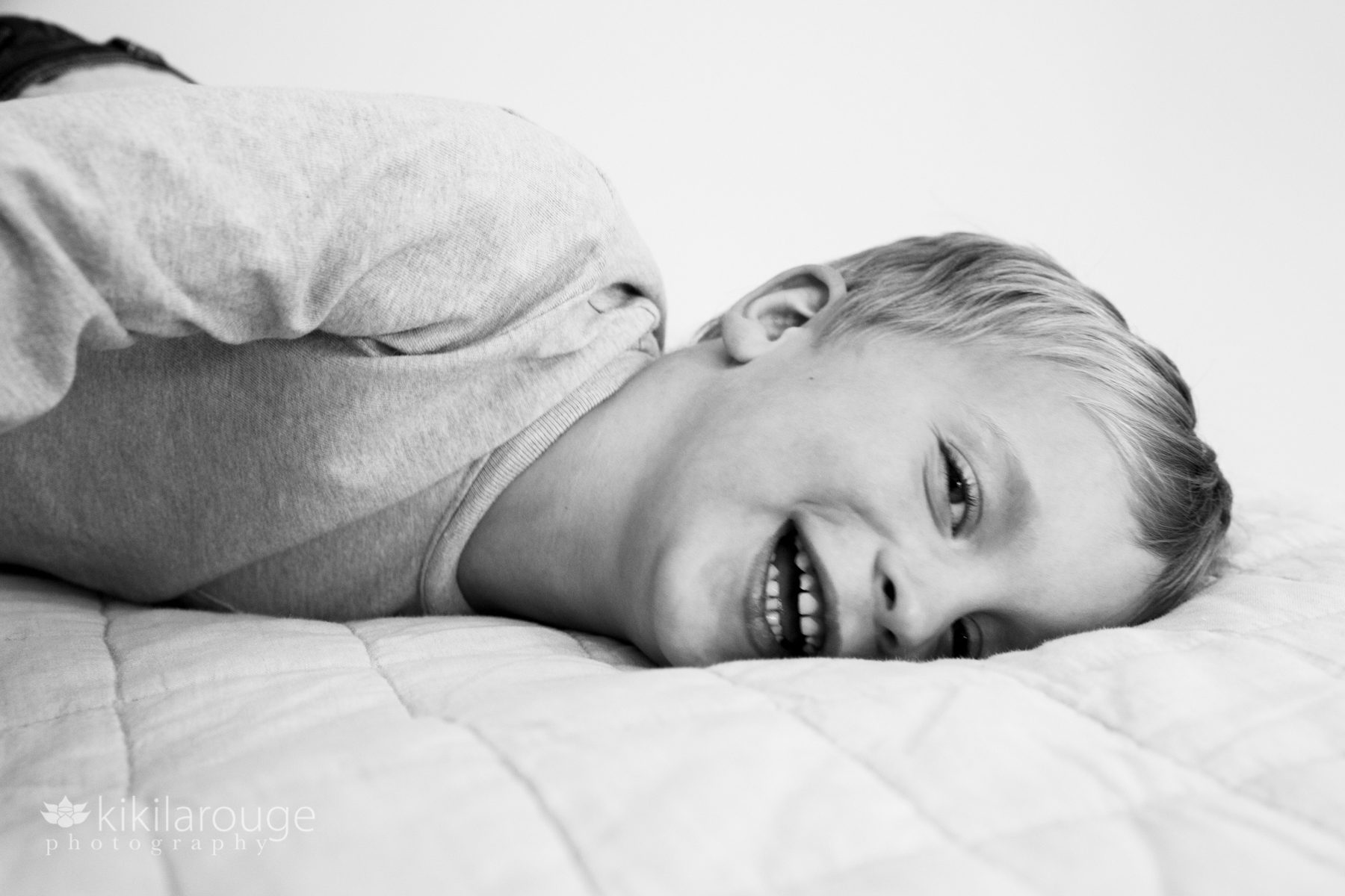 Young boy laying down and laughing on big bed