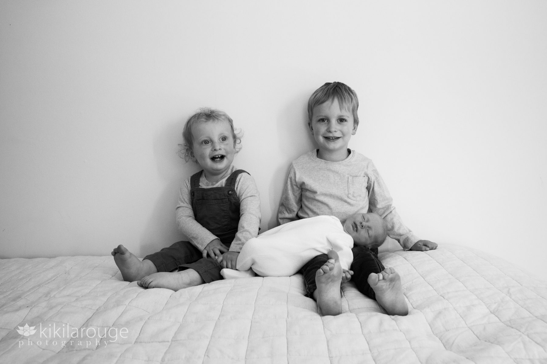 Two little boys with their newborn baby sister on bed