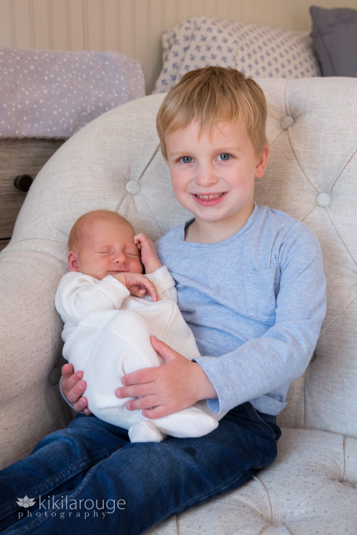 Young boy blonde hair holding his newborn baby sister in big chair