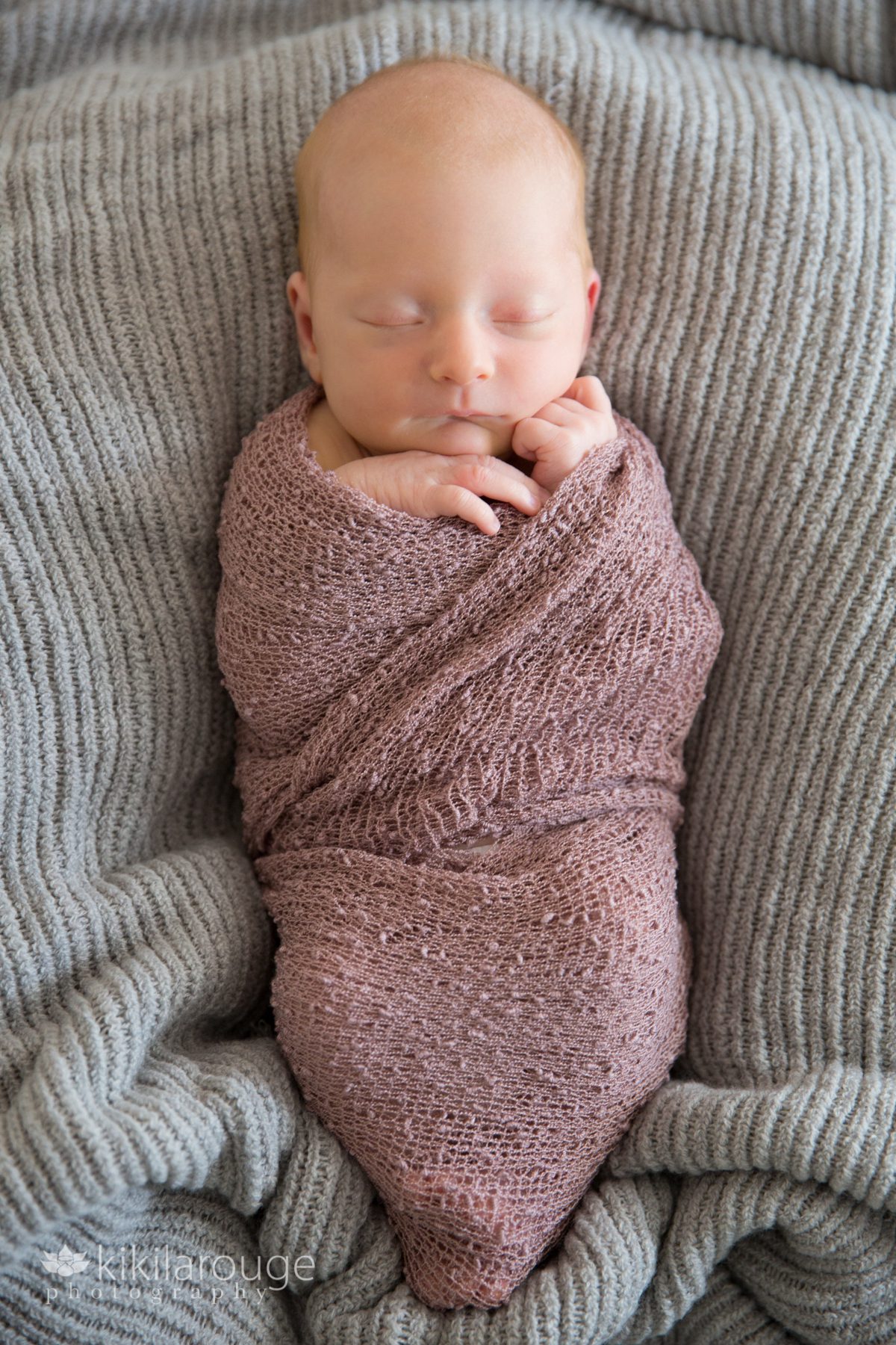 Sleeping newborn baby wrapped in purple wrap on gray blanket
