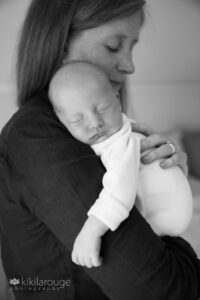 Mom holding sleeping newborn in white sleeper
