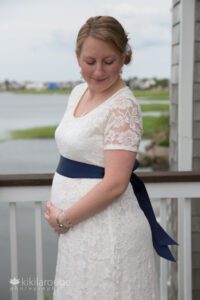 Pregnant bride in lace dress and blue sash looking down