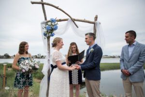 Couple getting married under driftwood altar by the water