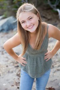 Blonde girl green embroidered top and jeans leaning and smiling into the camera