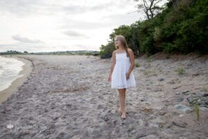Teen girl in white dress walking at beautiful beach looking to the side