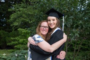 Tall girl in cap and gown hugging mom with glasses and red hair