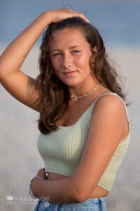 Girl with tan and long brown hair at beach with hand in hair