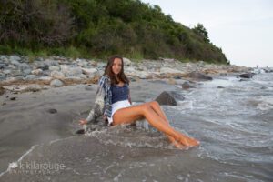 Senior portrait girl in plaid shirt and white shorts sitting at waters edge