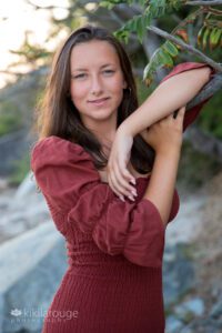 Teen gril in maroon dress at beach leaning on branch posing
