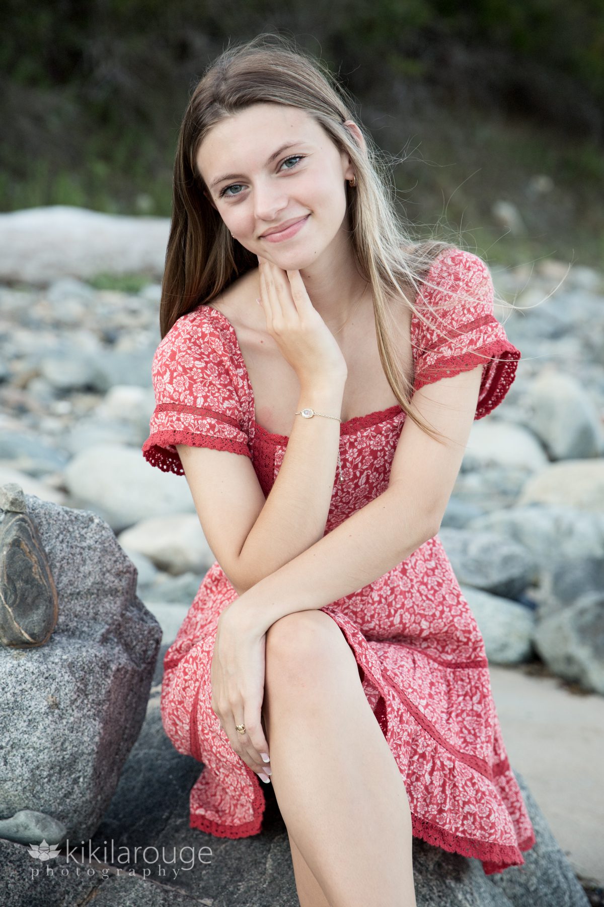 Teen girl in pretty read dress sitting on rocks at beach