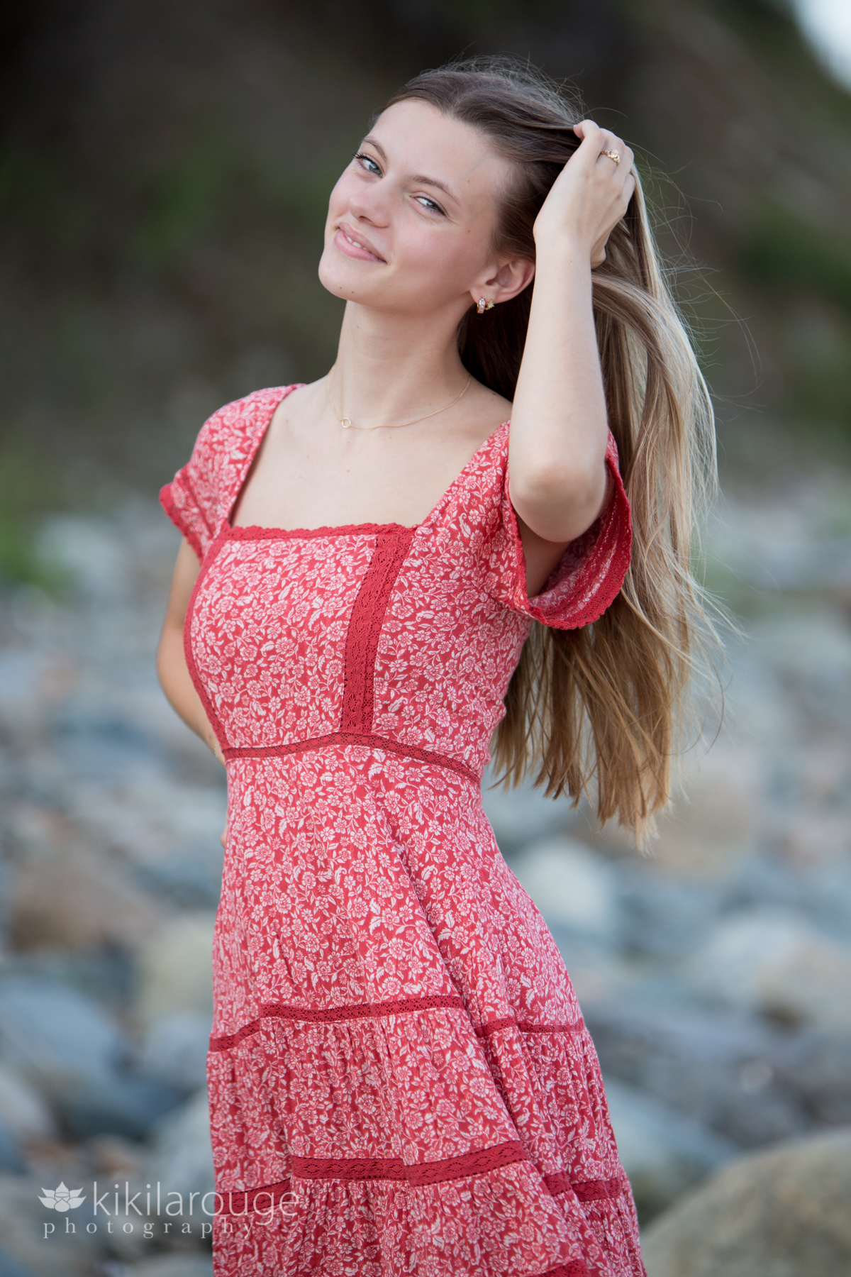 Teen girl smiling hand in long hair in red dress at beach