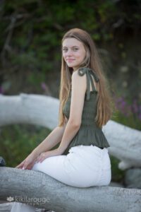 Teen girl long blonde hair in green top and white jeans sitting on driftwood