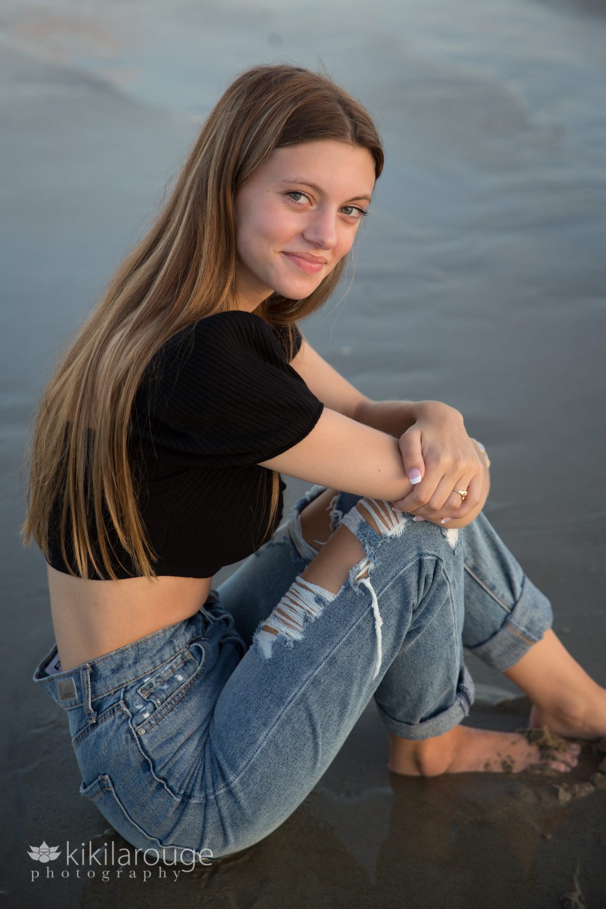 Girl sitting in beach water in ripped jeans and black top