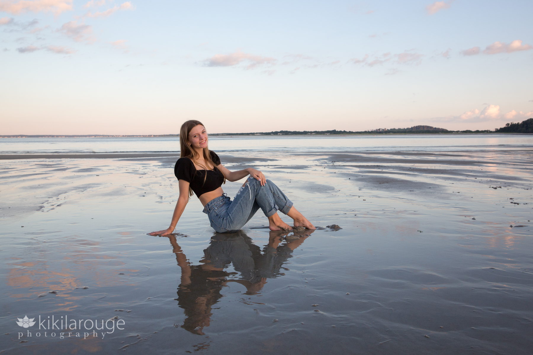 Senior girl sitting in water at beach with reflection and sunset