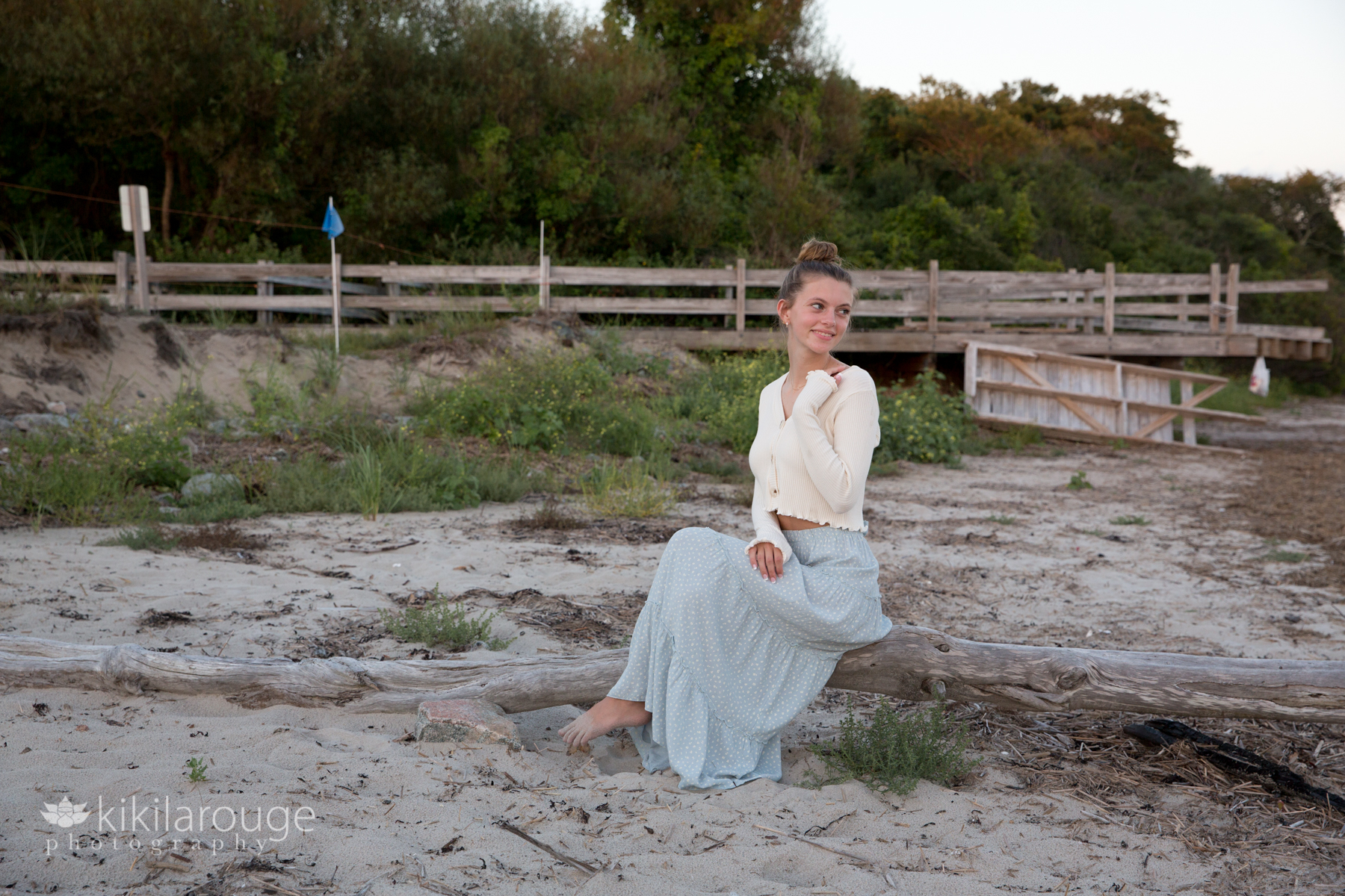 Teen girl sitting on driftwood at beach with blue skirt