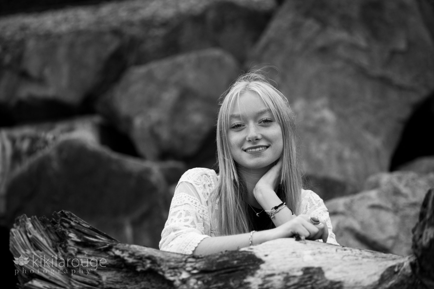 Teen with blonde hair leaning and smiling on large driftwood