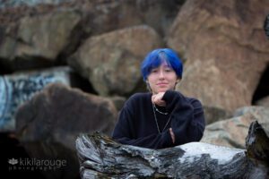 Teen looking serious on driftwood with blue hai